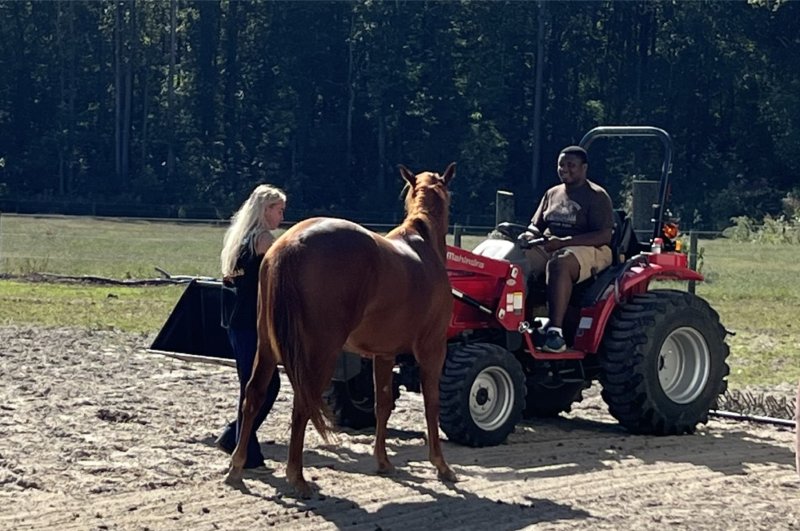 Veteran Kanye Reid tries to drive a tractor as Bekah Baughman, a facilitator at Courageous Hearts, leads therapy horse Cracker Jack away from the action.
